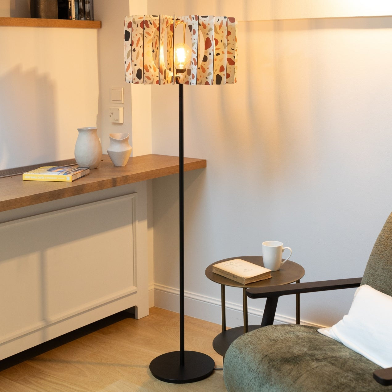 A floor lamp with a patterned shade, featuring a mix of white and orange terracotta tiles, standing in a room with ambient lighting.